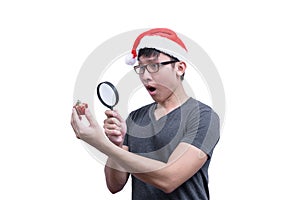 Asian Santa Claus man with eyeglasses and grey shirt has searching and looking a red gift box with magnifying glass isolated on w