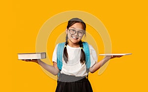 Asian School Girl Comparing Digital Tablet And Book, Yellow Background