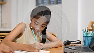 Asian school girl distance learning online, doing homework while sitting at kitchen table