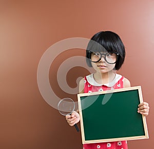 Asian school kid hold a chalkboard and magnifying glass