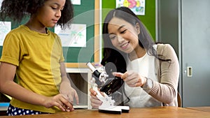 Asian school teacher helping students use microscope