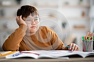Asian schooler chubby boy dreaming about something while doing homework