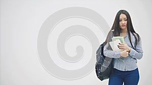 An asian schoolgirl appearing on a white background with a backpack slung over her shoulder, holding a stack of books