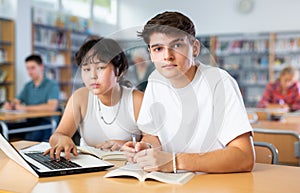 Asian schoolgirl with classmate guy, studying on a laptop and making notes in a copybook