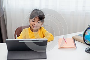 Asian schoolgirl doing her homework with digital tablet at home. Children use gadgets to study. Education and distance learning