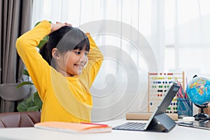 Asian schoolgirl doing her homework with digital tablet at home. Children use gadgets to study. Education and distance learning