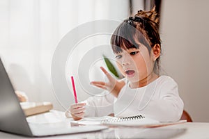Asian schoolgirl doing her homework with laptop at home. Children use gadgets to study. Education and distance learning for kids.