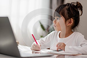 Asian schoolgirl doing her homework with laptop at home. Children use gadgets to study. Education and distance learning for kids.