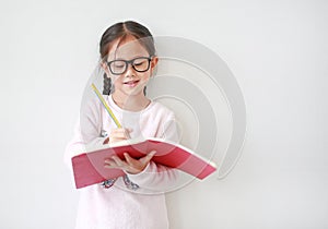 Asian Schoolgirl wearing eyeglasses holding and writes in a notebook with pencil on white background