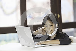 An Asian schoolgirl wears a mask and is studying online at home