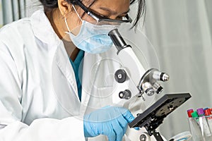 Asian scientist biochemist or microbiologist working research with a microscope in laboratory.
