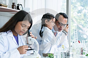 Asian scientist kid student and Indian teacher looking at plant in test bottle at biology class in school laboratory, do an