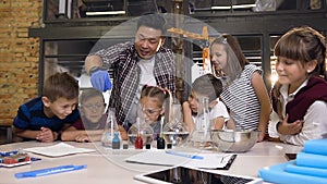 Asian scientist with six young children working with chemical reaction in chemistry lab. Chemical reaction blue color in