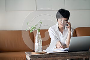 Asian self employed woman sitting on couch & working on laptop at home