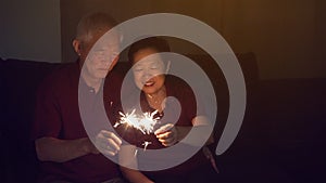 Asian senior couple celebrating together at home sparkles firework s