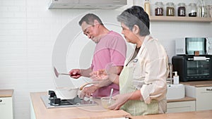 Asian senior couple cooking together in kitchen, Making eggs for breakfast