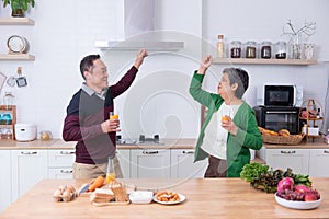 Asian senior couple is dancing and smiling while cooking together in the kitchen counter