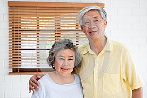 Asian senior couple embrace togerther and looking at camera in living room at home.Happy retirement lfie.aging at home concept