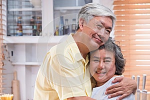 Asian senior couple embrace togerther and looking at camera and smiling in kitchen at home.Happy aging at home concept