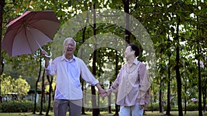 Asian senior couple have fun rainy season red umbrella in green park