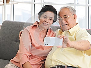 Asian senior couple having good time together,sitting in living room , talking selfie photo or video chatting looking at  smart