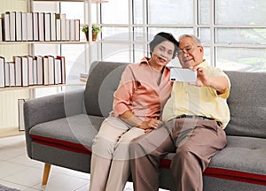 Asian senior couple having good time together,sitting in living room , talking selfie photo or video chatting looking at  smart