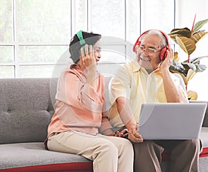 Asian senior couple having goodtime together , listen to the music from headphones with computer laptop on lap. Elderly lifestyle