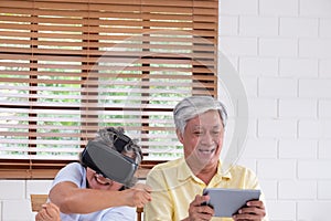 Asian senior couple play virtual realtiy glasses headset and tablet watching vr video and  have fun together in living room at