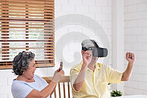 Asian senior couple play virtual realtiy glasses headset and tablet watching vr video and  have fun together in living room at