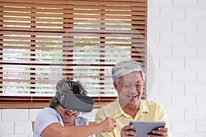 Asian senior couple play virtual realtiy glasses headset and tablet watching vr video and  have fun together in living room at