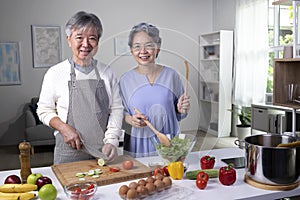 Asian senior couple preparing food in the kitchen. Retired people cooking meal at home, looking at camera