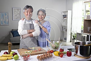 Asian senior couple preparing food in the kitchen. Retired people cooking meal at home, looking at camera