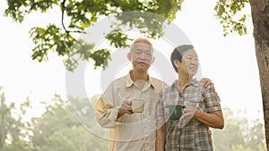Asian senior couple relax drinking coffee in summer park, green