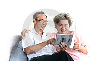 Asian senior couple sit on sofa enjoy using tablet. Retired people smiling
