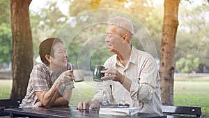 Asian senior couple start morning coffee in park, optimistic and