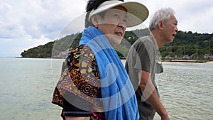 Asian senior couple tourist in Thailand sea Summer trip walking in shallow sea from boat to resort fun tropical holiday