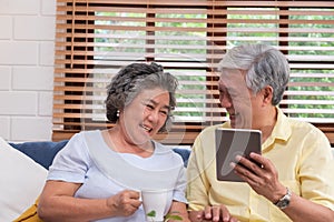 Asian senior couple using table compute and drink coffee sitting at sofa in living room at home.senior with technology lfiestyle.a photo