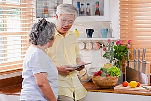 Asian senior couple using tablet computer to searching menu recipe and type of vegetable in kitchen at home.senior with technology