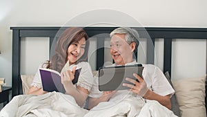 Asian senior couple using tablet at home. Asian Senior Chinese grandparents, husband watch movie and wife read book after wake up