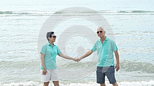 Asian senior couple walking together on the beach by the sea