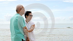 Asian senior couple walking together on the beach by the sea