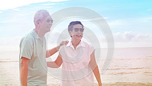 Asian senior couple walking together on beach by the sea