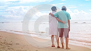 Asian senior couple walking together on beach by the sea