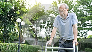 Asian Senior disabled man walking slowly with walker or cane at park. Older elderly mature handicapped patient male feeling