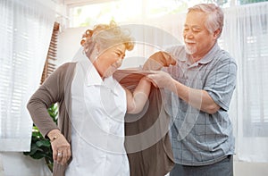 Asian senior elder man help elder woman wear a shirt at home