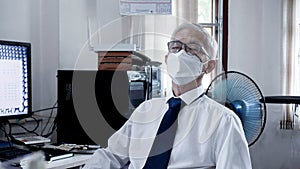 Asian senior elder man working on computer exhaustly at work from home office wearning mask and glasses