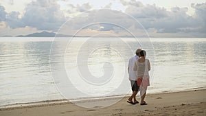 Asian senior elderly couple hugging walking on sunrise beach sea background together happiness concept