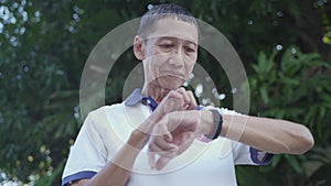 Asian senior elderly man touching smart watch activity tracker at park under tree. finger tapping sport watch for calories and hea