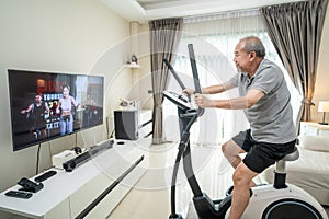 Asian Senior Elderly man workout cardio on cycling exercise bike machine at home for well being. Active Older male doing lockdown