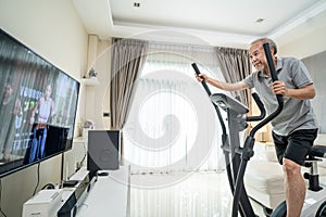 Asian Senior Elderly man workout cardio on cycling exercise bike machine at home for well being. Active Older male doing lockdown